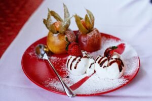Red plate with creamy dessert, strawberries, and two sugar-dusted apples - a delectable treat.