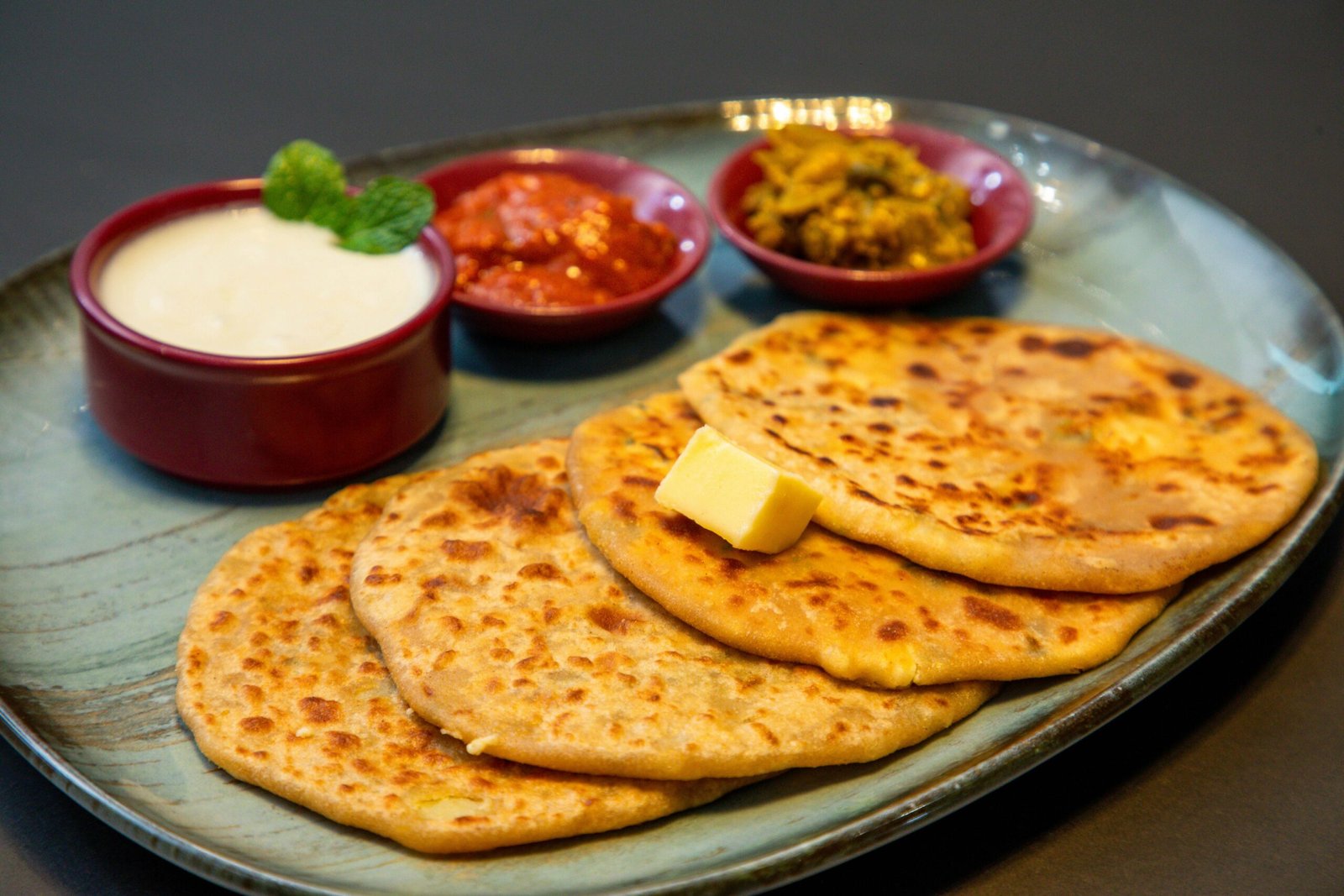 Appetizing Indian paratha served with yogurt and pickles on a blue plate.